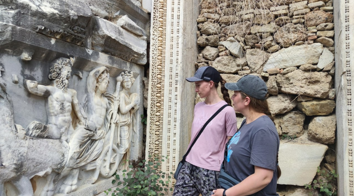 Readers of Aleksei Meniailov study a bas-relief with a story about the god Dionysus in an ancient amphitheater during a joint tourist trip with the writer to the city of Perga